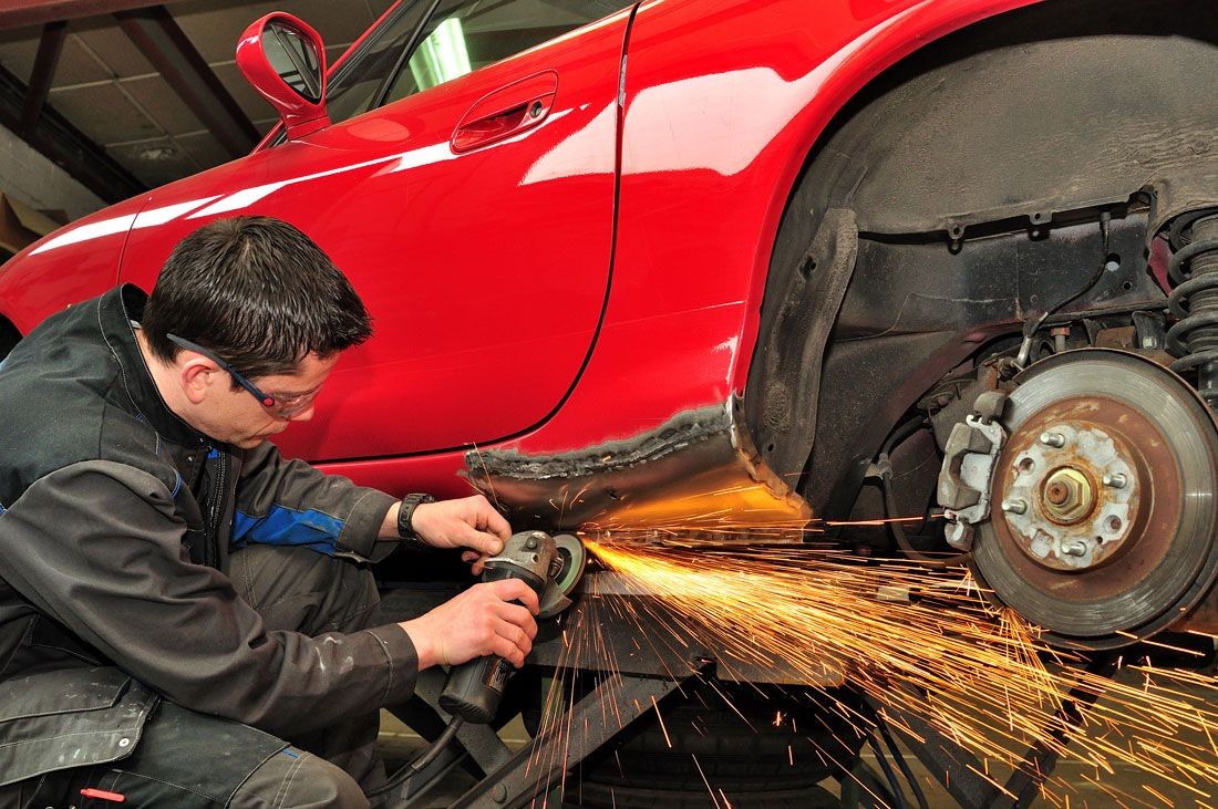 Mechanic grinding the body of a red car, producing sparks in an auto repair shop.